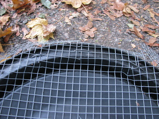 Photo of the edge of the lid, with mesh protruding over
the edge, and wire periodically coming up through the plastic
and mesh and down again a few centimeters farther around the
rim.