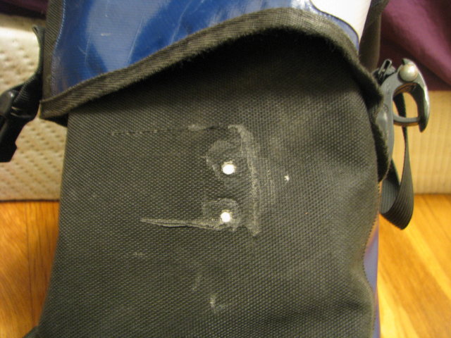 The outside of the bag, where the fabric is disrupted in 3 lines (the 3 edges of the hole). Two small gray circles are visible where the patch shows through from the inside. The fabric is a little cloudy in places, perhaps where solvent leaked through.