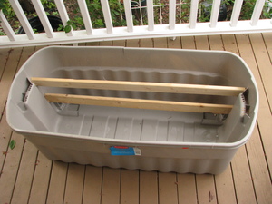 3/4 top view into a long rectangular beige plastic tub. Two pieces of wood have been inserted, running lengthwise, pressure-fit against the far ends.