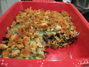 Red ceramic casserole dish showing a casserole that's about half millet and half other things, topped with cheese and croutons. There's a green spice mix on the cheese.